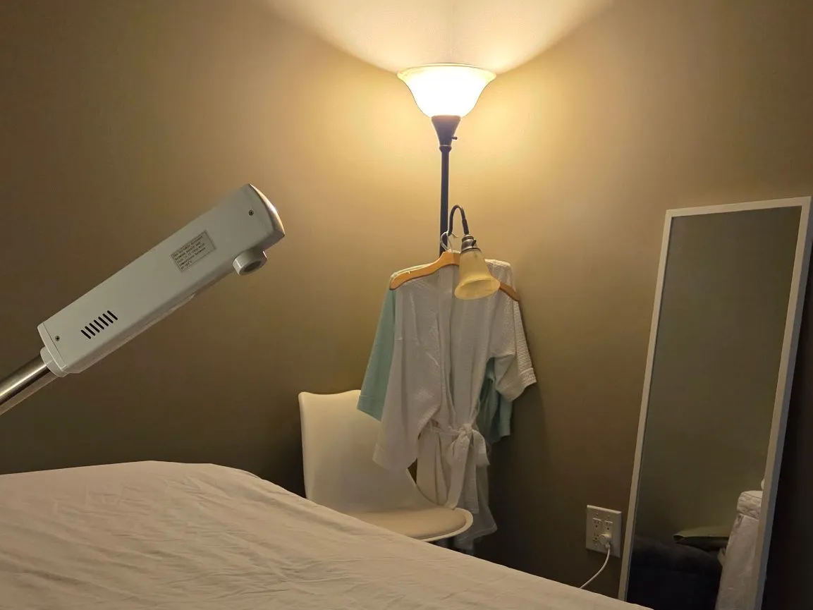 Treatment bed with a robe, chair and floor lamp in the corner of the room